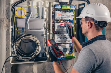 Man, an electrical technician working in a switchboard with fuses. Installation and connection of electrical equipment. Professional uses a tablet.